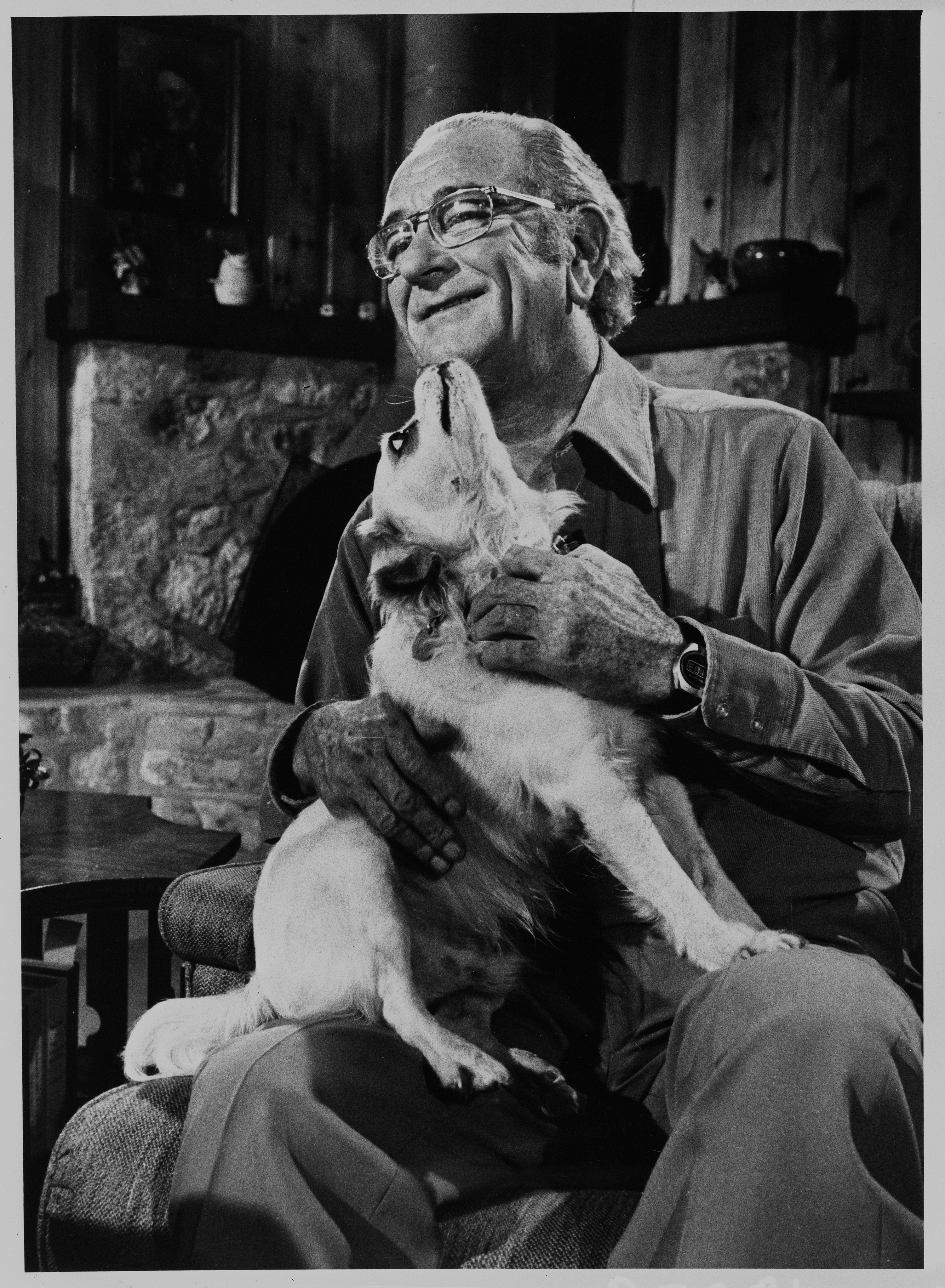 President Johnson, in casual attire and glasses, sits at home with his dog Yuki in his lap. 